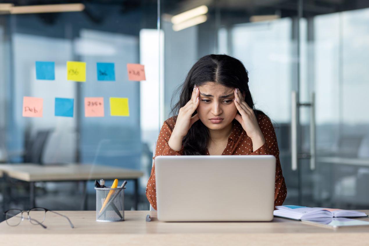 Eine gestresste Frau im Büro hält sich den Kopf – Mobbing und Arbeitsstress sind ernstzunehmende Probleme. Ein Anwalt für Arbeitsrecht kann Betroffenen helfen.